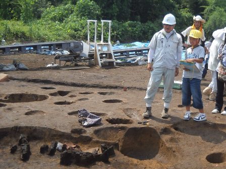 発掘作業現場で調査職員から話を聞いている様子の写真